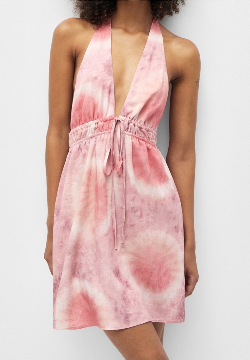 Vestido halter rosa y blanco sin mangas, con un profundo escote en V y una cintura ajustada con un delgado cordón, llevado por una persona de pie.