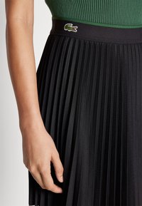 Gonna nera plissettata realizzata in tessuto testurizzato, con una fascia verde a contrasto e un piccolo logo ricamato di coccodrillo sulla vita.