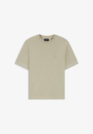 T-shirt beige clair à manches courtes avec col rond, texture subtile, petit logo brodé "SD" sur la poitrine et double rayures blanches sur les manches.