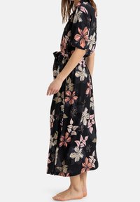 Robe maxi fleurie à manches courtes, en tissu noir, présentant de grandes fleurs roses et crème, taille ceinturée, design fluide, finition texturée.