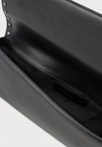 Must nagelaste rahakott, millel on sile tekstuur, avatud sektsioon ja külglabel. Sisepind on vooderdatud tumeda kangaga ja logoprindiga.