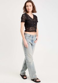 Un crop top en dentelle noire avec des manches courtes et un col festonné, associé à un jean droit taille haute bleu clair et des sandales noires.