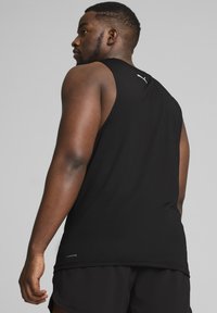 Camiseta de entrenamiento negra hecha de tejido transpirable, con un escote redondeado y el logo de Puma en la parte posterior. La textura se ve suave.