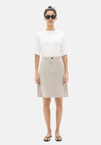 Chemise blanche à manches courtes associée à une jupe rayée longueur genoux avec une ceinture, des boutons décoratifs, et des tongs noires à enfiler.