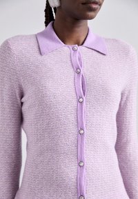 Purple knit cardigan with a textured finish, featuring a collar and decorative buttons. Smooth fabric and a slightly fitted silhouette.