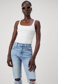 Top a righe bianco abbinato a jeans a vita alta di un blu chiaro con aree strappate sulle ginocchia. Il modello indossa occhiali da sole beige.