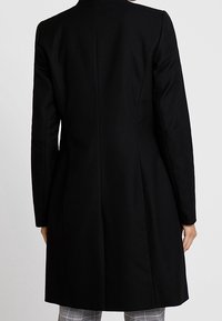 Manteau noir sur mesure avec une finition texturée, manches longues et une silhouette structurée. Comprend des détails de couture au centre et un design épuré.