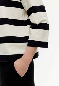 Top de algodón a rayas blancas y negras con mangas tres cuartos y dobladillo redondeado, con un puño ancho negro y detalle de bolsillo lateral.