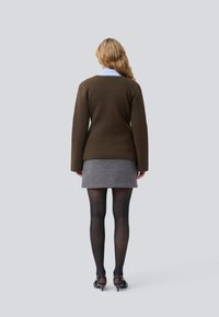 Brun trøje med lange �ærmer, parret med en struktureret houndstooth-nederdel. Model iført sorte tætsiddende strømpebukser og høje sko.
