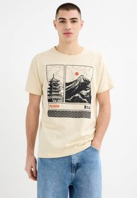 Camiseta de manga corta beige con estampados gráficos en negro de una pagoda y el Monte Fuji, con acentos de sol rojo y un borde con patrón de olas.