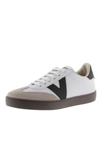 Vit sneaker med grå mocka framkappa, svarta läderdetaljer och mörkbrun sula. Har snörningsdesign och V-formad logotyp på sidan.