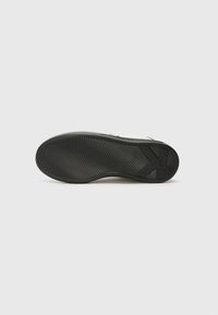 Zwarte rubberen loopzool met een gestructureerd golfpatroon. Bevat een opvallend logo en een lichte curve bij de hiel voor verbeterde grip en flexibiliteit.