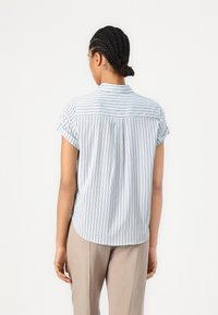 Camicetta azzurro chiaro a maniche corte con righe verticali bianche, colletto a bottoni e orlo arrotondato. Tessuto liscio con vestibilità casual.