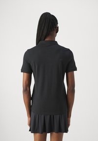 Černé polo tričko s krátkými rukávy, texturovaná látka a rozšířený lem. Jednoduchý design límce. Zadní pohled ukazuje hladkou siluetu.