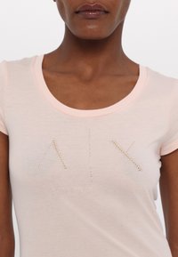 Lichtroze, aansluitend T-shirt met een ronde halslijn, verfraaid met metalen gestanste letters "AIX" in verticale opstelling. Zachte katoenen stof.