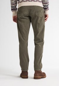 Pantalones de pana en verde oliva con corte recto, que cuentan con bolsillos traseros y se combinan con botas de tobillo marrones. Superficie texturizada visible.