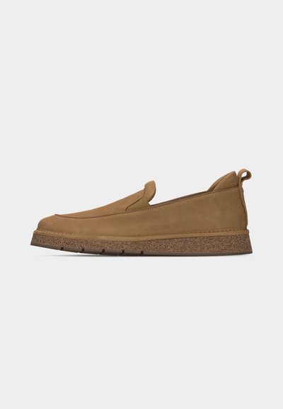 Chaussure à enfiler en daim beige avec semelle marron texturée, panneaux latéraux élastiques et languette à l’arrière, présentée de profil sur fond blanc.