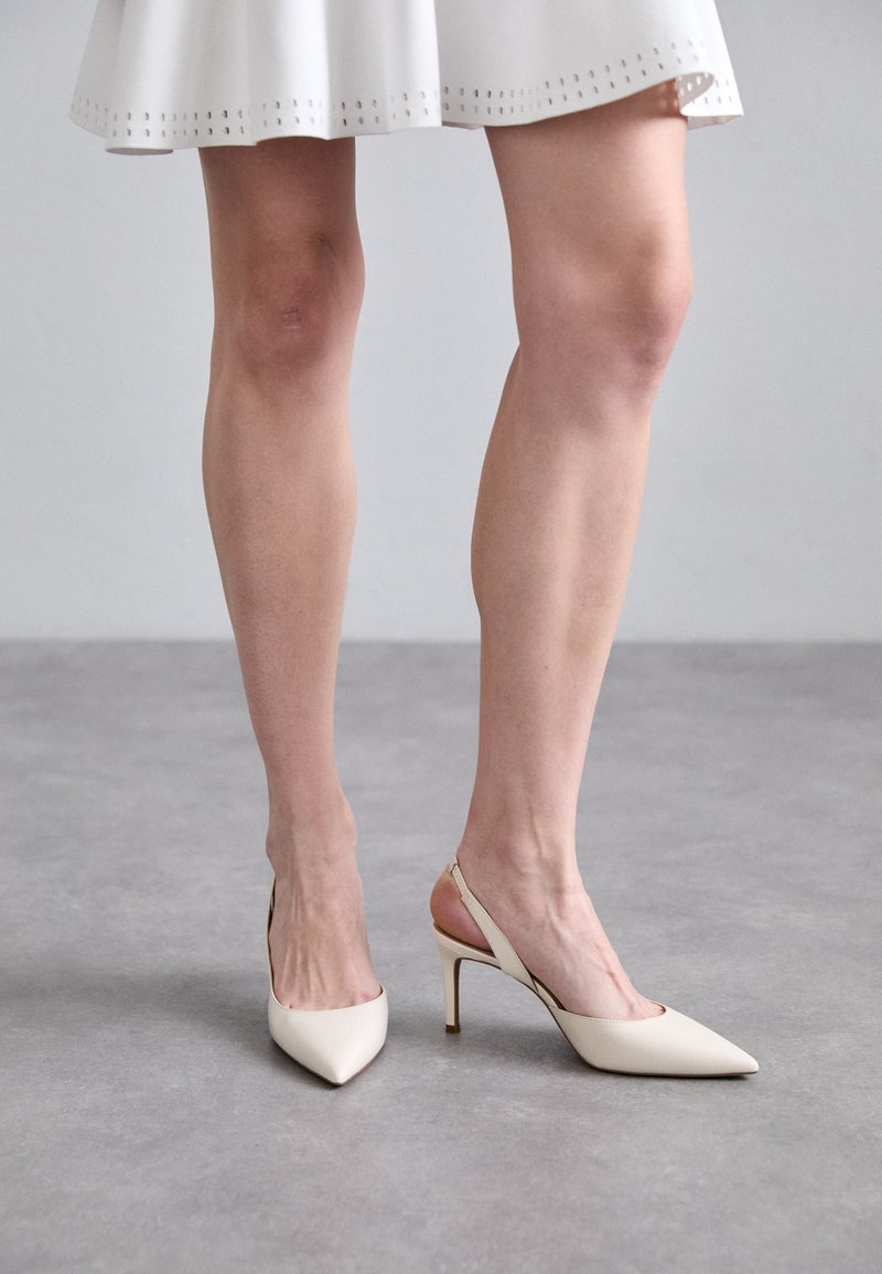 Ljusbeige slingback-klackar med spetsiga tår och blank finish. Har en tunn, hög stilettklack och en minimalistisk design.