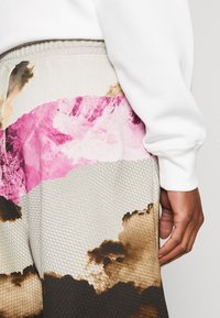 Los joggers texturizados presentan un diseño en bloques de color con tonos rosas, marrones, crema y grises, cinturilla elástica y detalles de costura visibles.