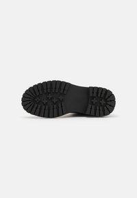 Semelle de chaussure en caoutchouc noir avec de profondes rainures et des stries rectangulaires pour une meilleure adhérence. Présente des bords arrondis et une zone centrale lisse.