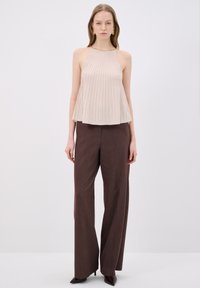 Beige geplooide haltertop met een textuurafwerking, gecombineerd met hoge, brede bruine broeken en pumps met een spitse neus.