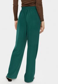 Pantalons larges verts en tissu lisse avec une taille élastique, présentant une coupe décontractée et sans motifs ni accents visibles.