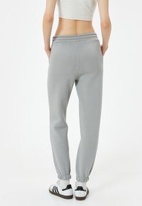 Lichtgrijze sweatpants met een trekkoord in de taille, taps toelopende enkels en een soepele textuur, gecombineerd met wit- en zwartkleurige sneakers.