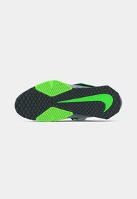 Sola de sapatilha atlética preta e verde com padrão de aderência texturizado, apresentando um grande logotipo Nike verde estilizado e elementos de tração segmentados.