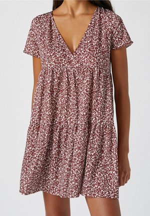 Femme portant une robe à manches courtes, col en V, ample avec un motif floral abstrait bordeaux et blanc.