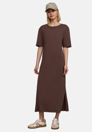 Mujer con vestido midi marrón de manga corta y detalles de botones en el hombro, gorra beige y zapatillas deportivas crema.