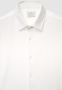 Chemise blanche boutonnée en tissu texturé avec un col italien, dotée de boutons blancs et étiquetée "CALLIOPE" avec la taille "L".