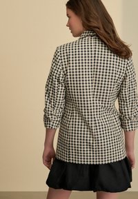 Svartvit gingham-blazer med skräddarsydd passform, enfaldig design och upprullade ärmar, parat med en svart rufflekjol.