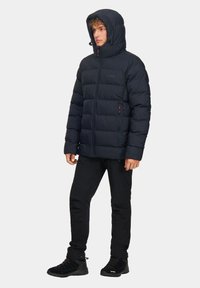 Granatowa kurtka puchowa z zamkiem z przodu i regulowanym kapturem, z pikowanymi sekcjami i dwoma bocznymi kieszeniami, zestawiona z czarnymi spodniami i butami.