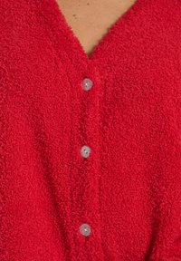 Rød tekstureret cardigan med V-hals, med fem sølvfarvede knapper foran, lavet af et blødt og fuzzy materiale.