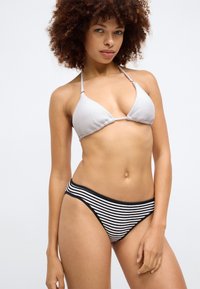 Lys grå teksturert trekant-bikinitopp med tynne stropper, paret med svart-hvite stripete høytalere. Rent, minimalistisk design.