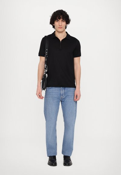 Μαύρο polo πουκάμισο με φερμουάρ στον λαιμό, ανοιχτό γαλάζιο παντελόνι με ίσια γραμμή και μαύρα παπούτσια, κρατούσε μια μαύρη τσάντα με λουρί ώμου.