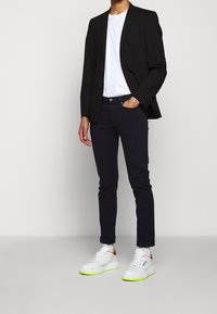 Svart kavaj, vit t-shirt, mörka jeans och vita sneakers med neongröna detaljer. Avslappnad men ändå prydlig outfit.