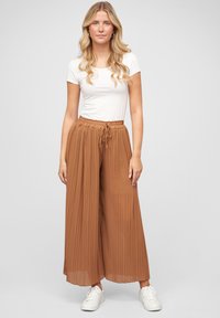 Lightweight, pleated brown trousers with an elastic waistband and drawstring. Paired with a fitted white t-shirt and white sneakers.