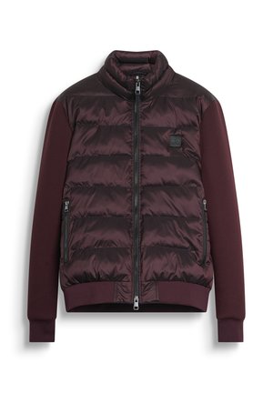 Bordeauxkleurige gewatteerde jacket met hoge kraag, ritssluiting en zijzakken. Beschikt over contrasterende stof en een merklabel op de borst.