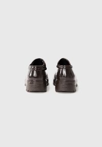 Scarpe in vernice nera con design arrotondato, suole in gomma elevate e texture liscia, caratterizzate da cuciture minime e senza hardware visibile.