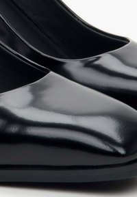 Czarne lakierowane szpilki z ostrym noskiem, gładką powierzchnią i niskim zapięciem, ukazujące elegancki, minimalistyczny styl.