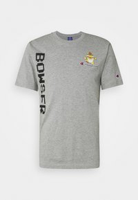 Šedé bavlněné tričko s grafikou Bowsera a logem "Champion". Obsahuje černý vertikální textový design na levé straně a žebrovaný kulatý výstřih.