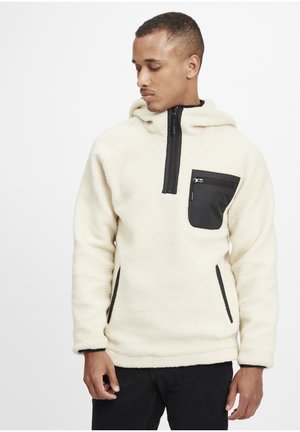 Cream fleece pullover with black zippered chest pocket and side pockets. Features a high collar and adjustable hood. Soft, textured material.