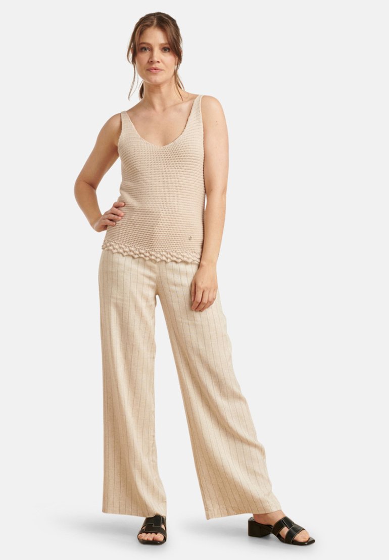 Beige gebreide tanktop met een ronde hals en een textuurpatroon, gecombineerd met wijde, gestreepte beige broek en zwarte instapsandalen.