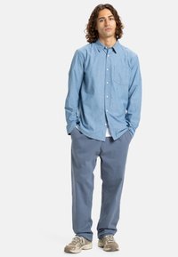 Camisa de botones de color azul claro con un bolsillo en el pecho, combinada con pantalones azul claro. La camisa tiene un corte holgado, y ambas prendas están hechas de una tela suave.