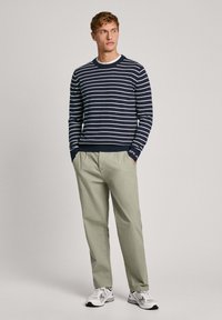 Navy prugasti pulover s bijelim horizontalnim prugama, okruglim izrezom i uskim rukavima; upareno s svijetlozelenim hlačama i sivim tenisicama.