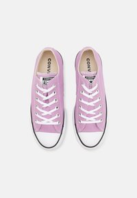 Różowe trampki z płótna z białymi sznurówkami, gumowym czubkiem i czarną podeszwą. Na języku znajduje się logo 'Converse All Star'. Klasyczny design.