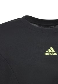Black t-shirt with a crew neck, made of stretchable fabric. Features a green Adidas logo on the left chest area.