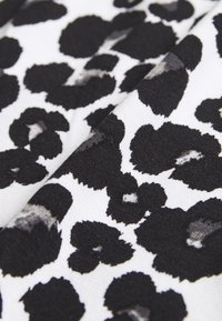 Tkanina w leopardzi wzór z dużymi czarnymi plamami na białym tle, o gładkiej teksturze i miękkim spadzie.