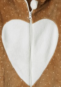Brown fleece garment with white polka dots and a large white heart shape in the center, featuring a white zipper and pom-pom pull.